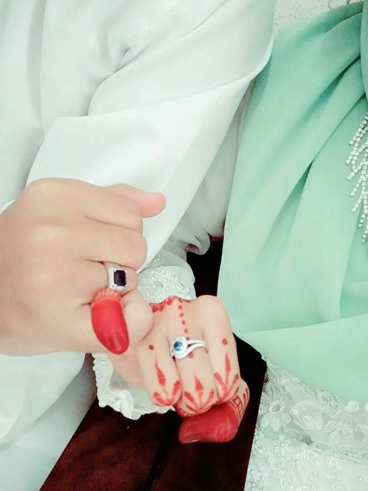 Couple’s hands wearing rings, with red henna and pale wedding attire