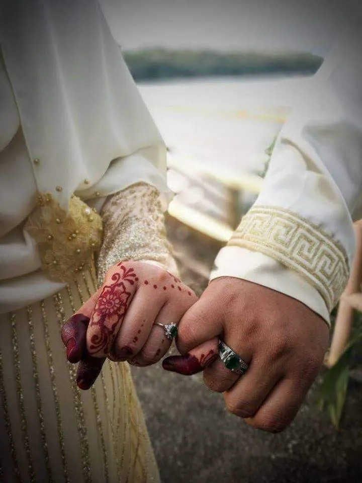 Joined hands with henna, rings, and embroidered wedding attire